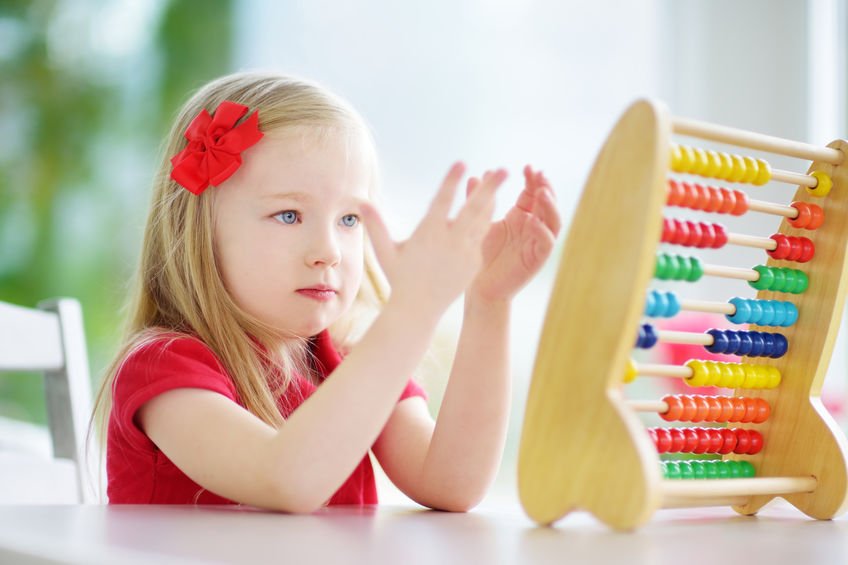 Cute little girl playing with abacus at home. Smart child learning to count. Preschooler having fun with educational toy at home or kindergarten.