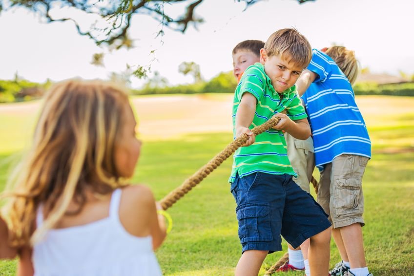 22168307 - group of happy young children playing tug of war outside on grass